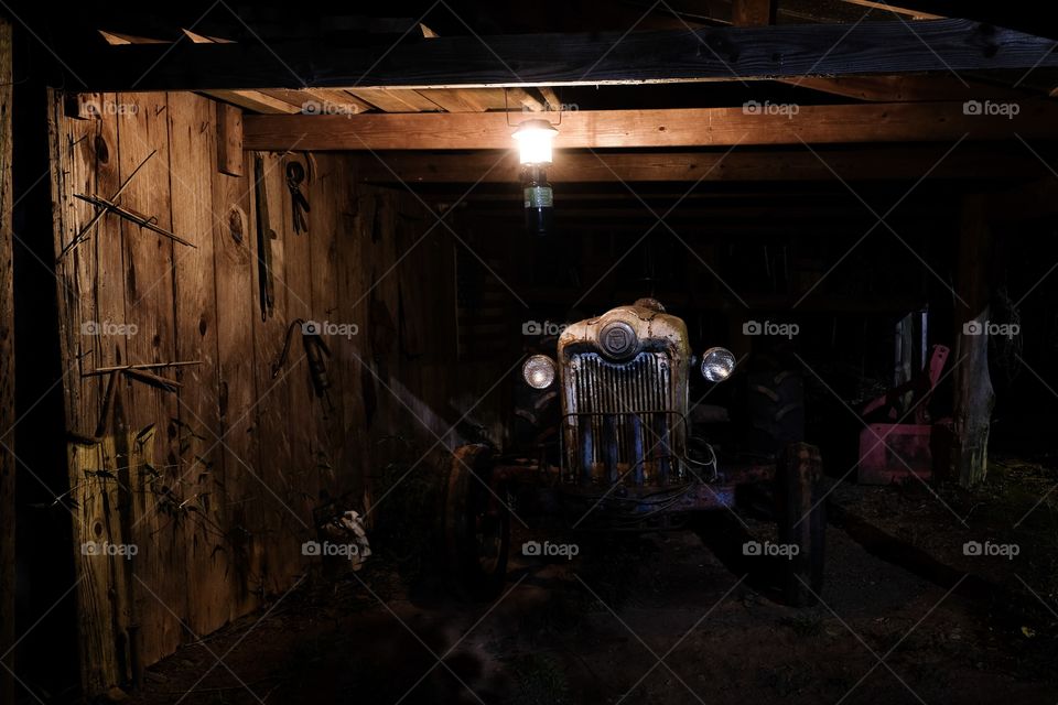 Front view of a 1953 Ford Jubilee vintage tractor that is still operational under the dim light of a lantern in an old barn. 