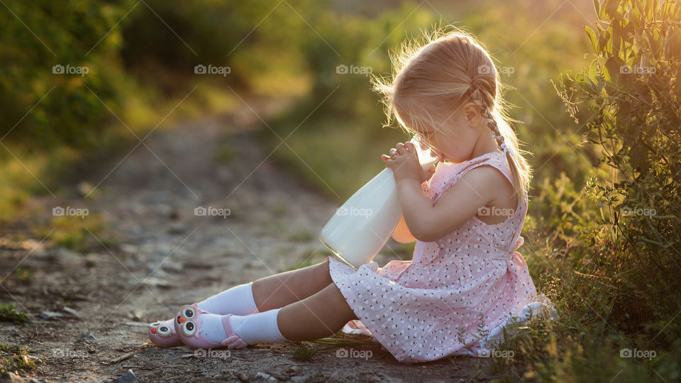 Little girl with blonde hair drinking milk outdoor 
