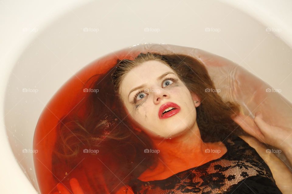 Girl lying in red water has an expression of extreme fear on her face; something horrible is happening