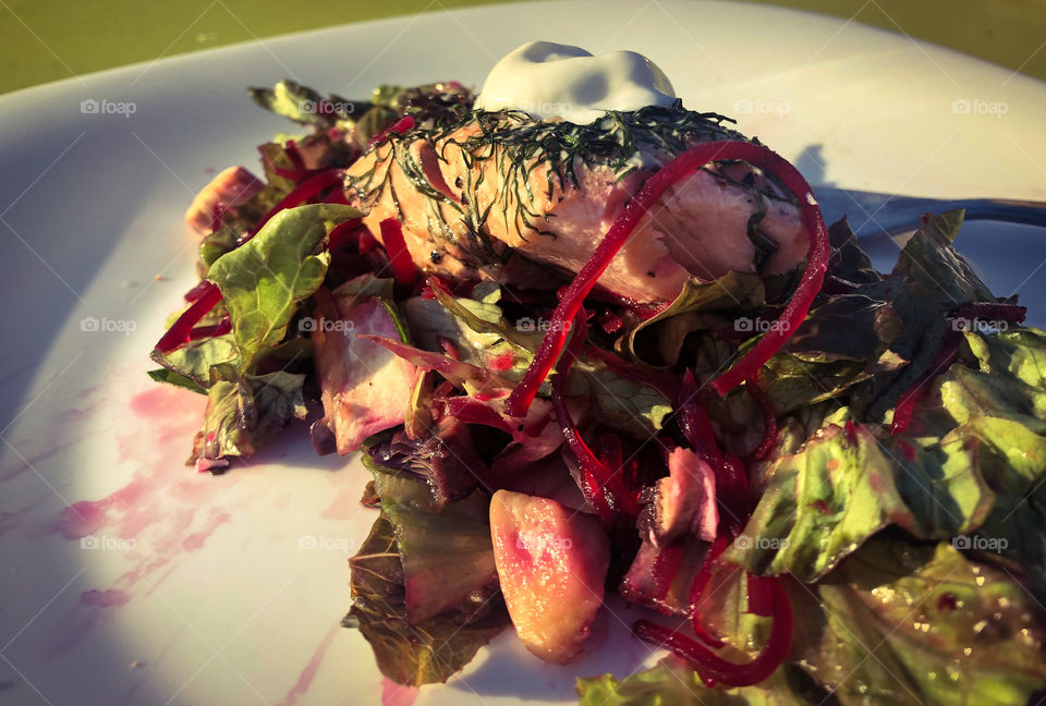 Beetroot salad and salmon topped with dill and a dollop of Greek yoghurt on a white plate