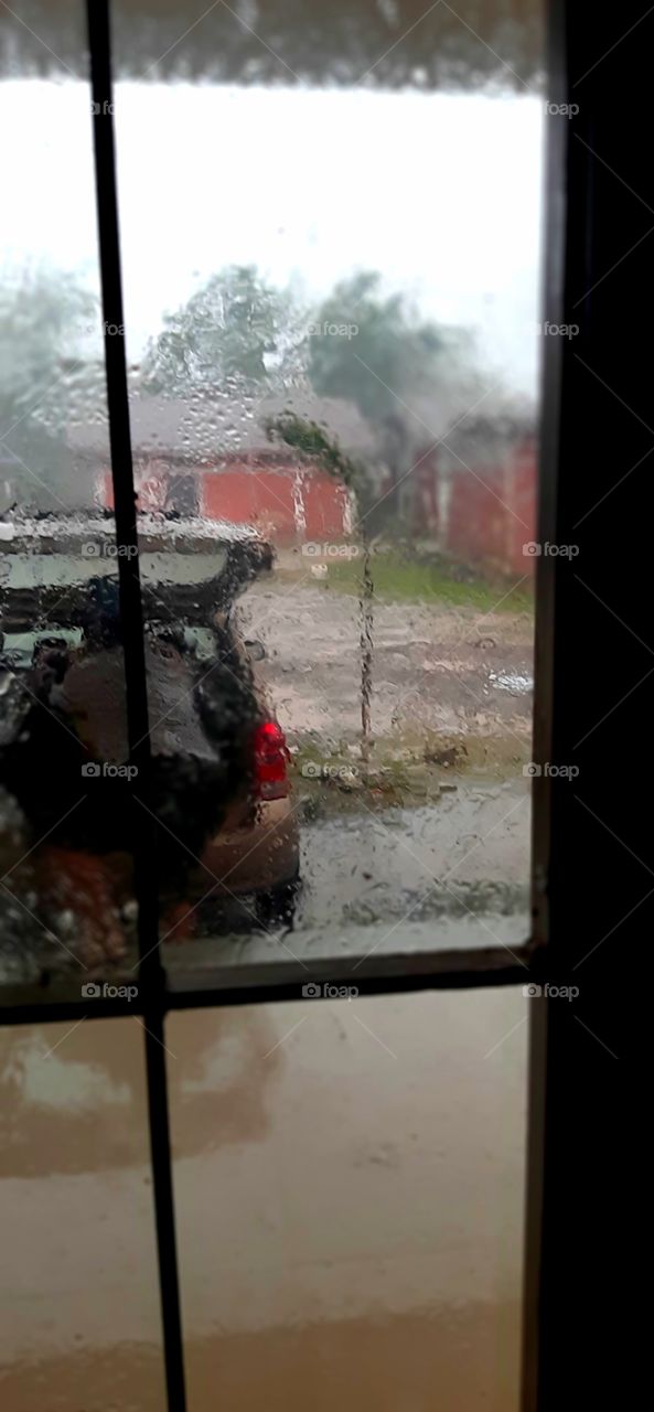 through safety indoor and through windows  a man outside in a storm can be seen opening rear door of car and the ground and window are wet with rain...perhaps the man too