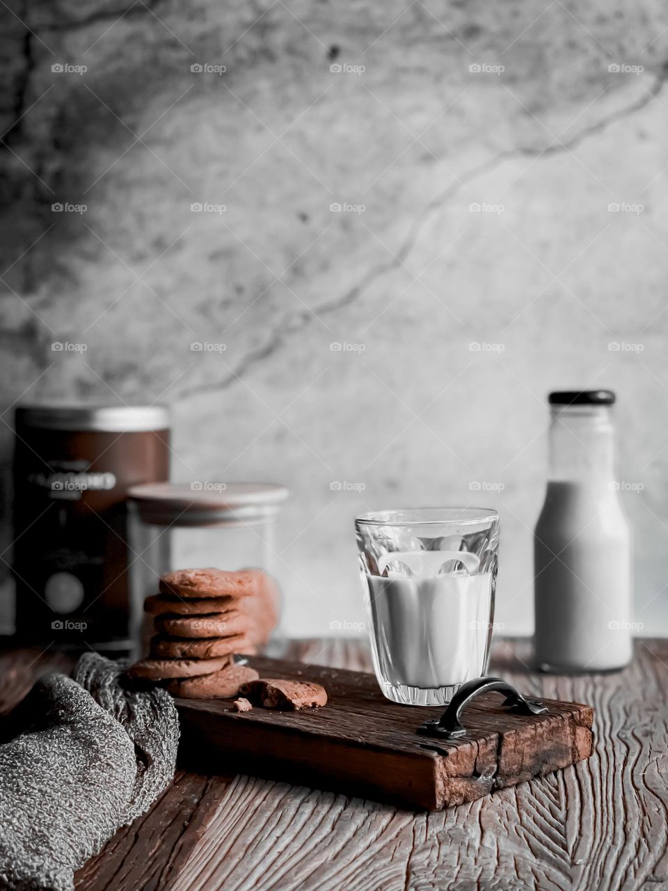 A warm cup of milk and a stack of biscuits on a wooden board and a bottle of milk at the back