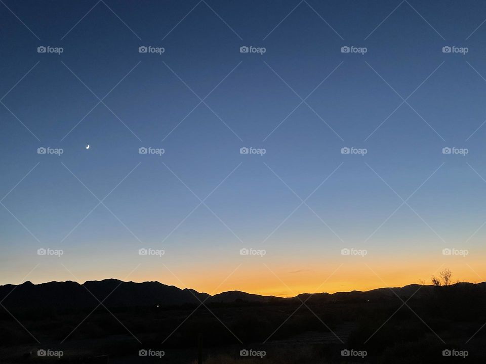 A orange sunset with the moon and mountains.