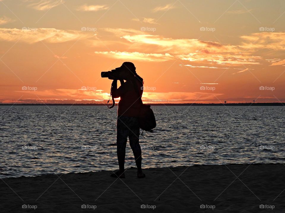 A photographer looking through the camera lens to catch the descending and colorful sunset 