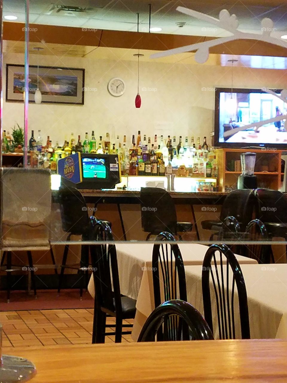 Bar, well stocked liquor bottles, video game, empty dining tables.