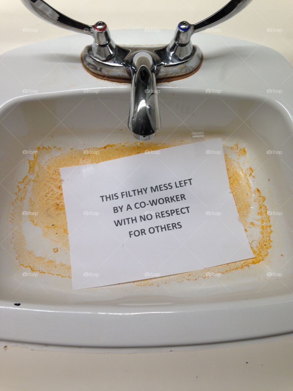 Angry sign "This filthy mess left by a co-worker with no respect for others" laying in filthy sink.