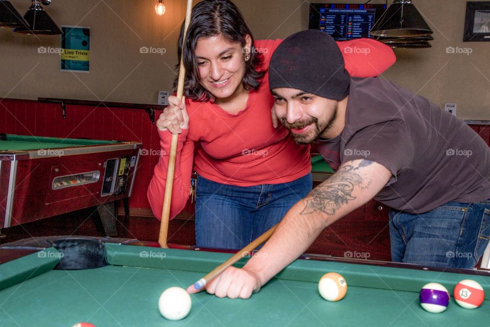 A couple enjoying an evening out playing pool at a pub. 