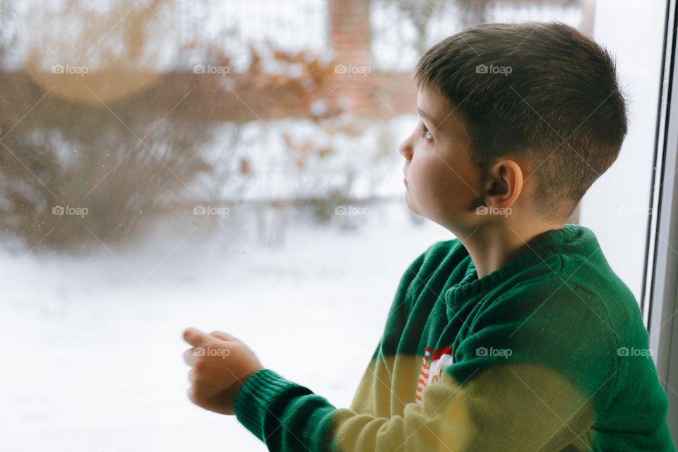 Cute curious teen boy looking through the window in the winter 