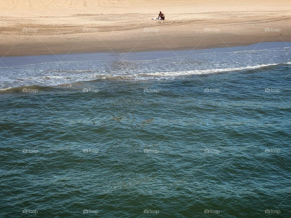 Lone figure sitting on a beach looking at the ocean waves 