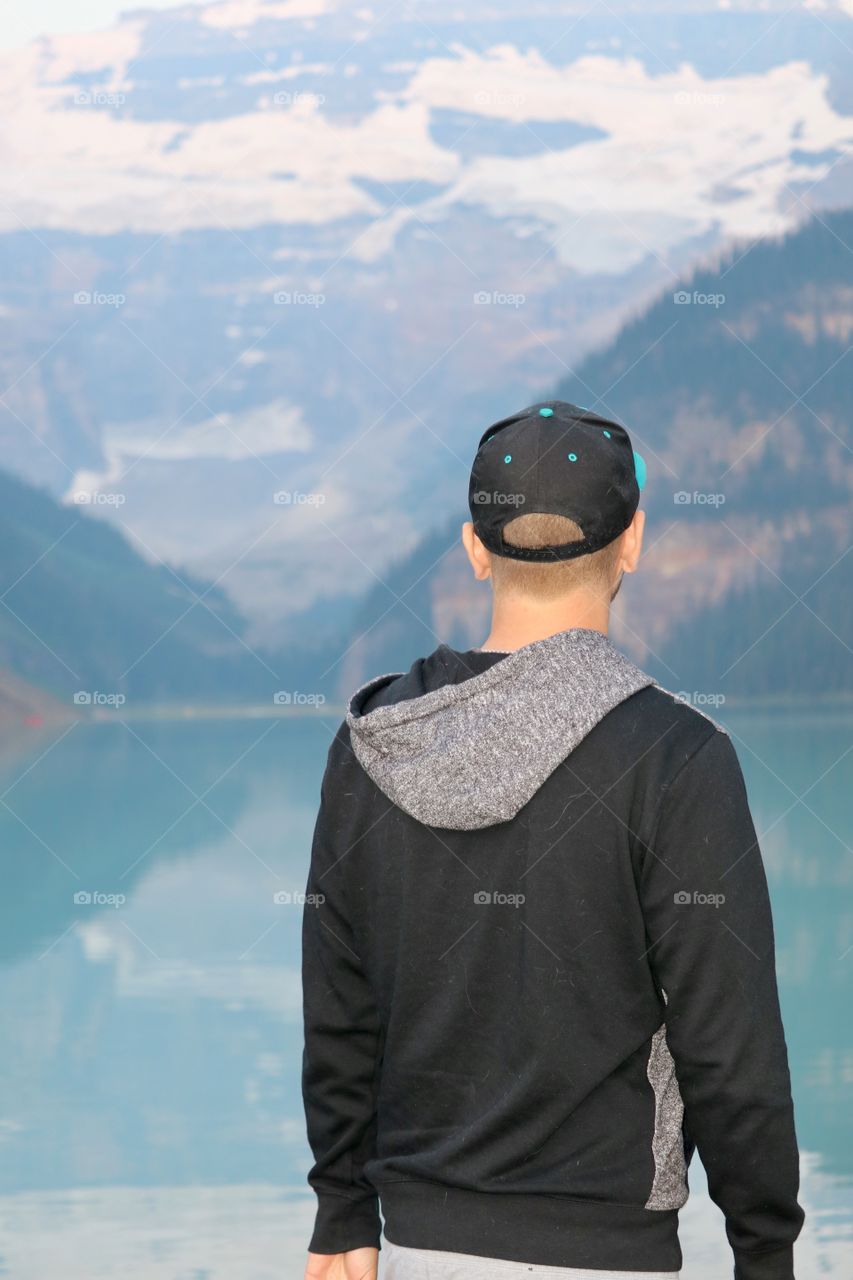 Young man wearing baseball cap and hoodie facing mountains at Lake Louise in the Canadian Rocky Mountains 