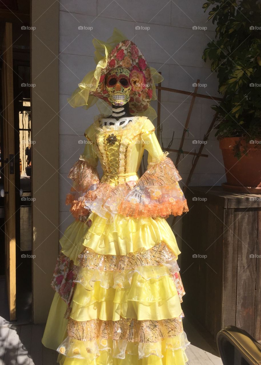 A skeleton decorated with a vivid floral dress and hat stands outside of a museum on Día de los Muertos.