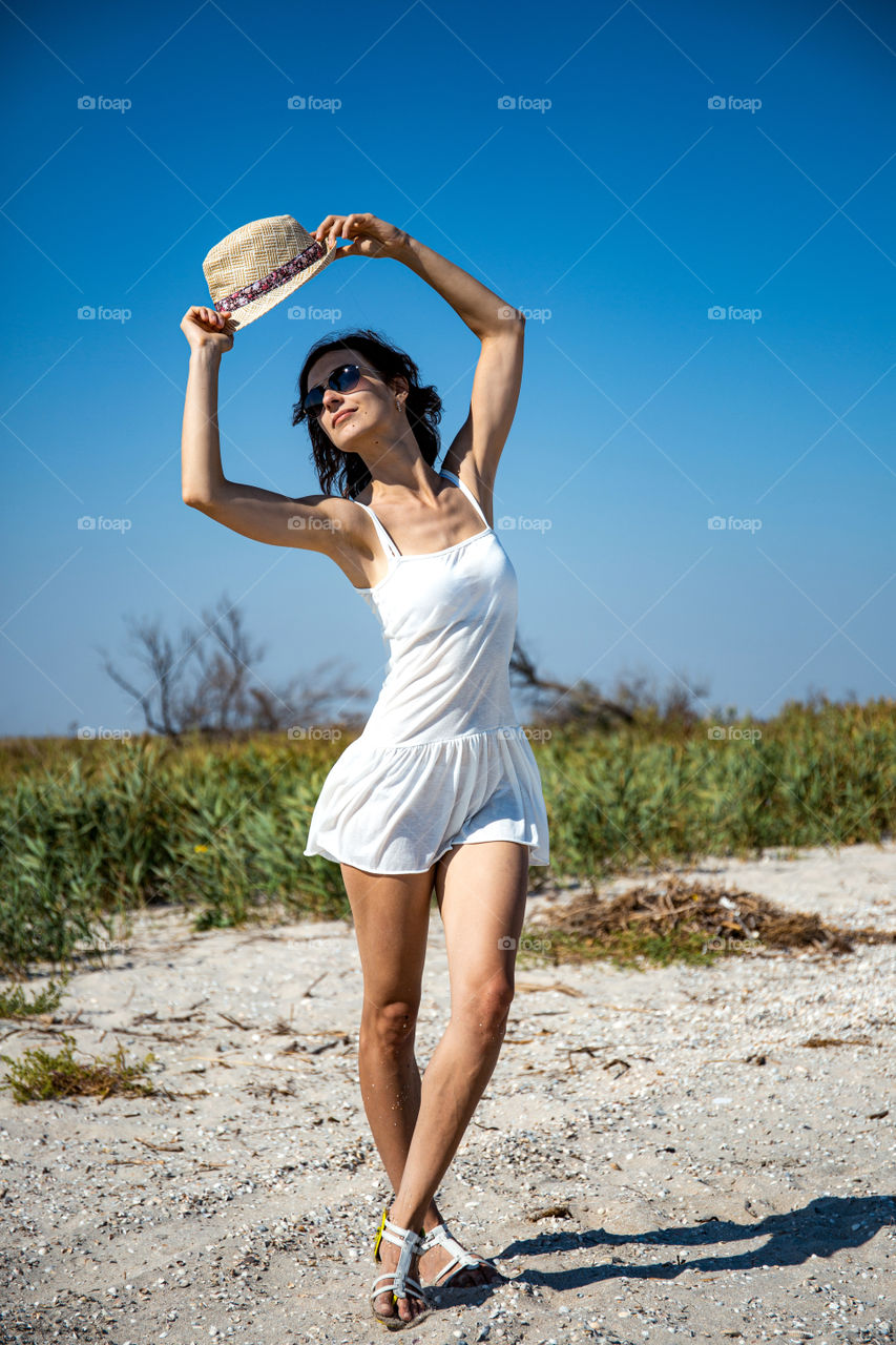 girl is dancing on the beach in short white dress, with hat. Joy mood and good shape