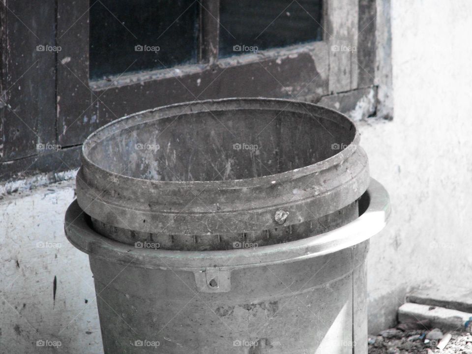 Gray trash cans sit near old windows and dull walls