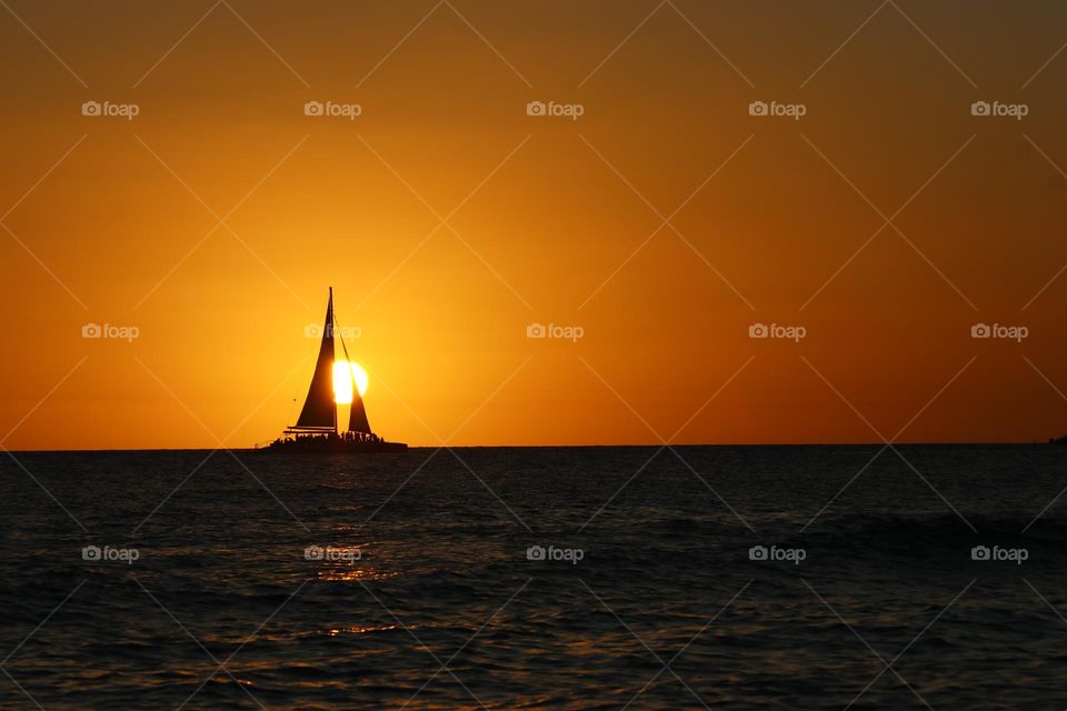 sailing boat crossing in front the sun at sunset