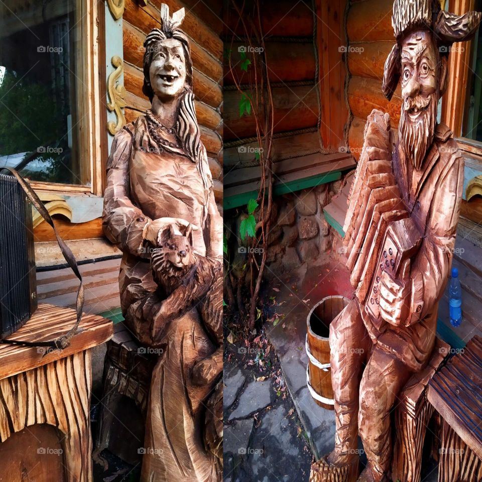 Happiness. Two photos in one. The first photo shows a wooden sculpture of a smiling grandmother sitting on a bench petting a cat. In the second photo there is a wooden sculpture of a smiling grandfather who plays the button accordeon