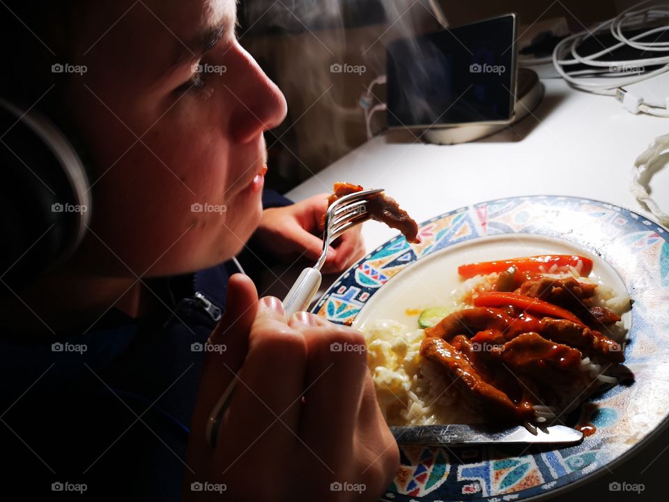 Teenager eating steamy hot supper while gaming on tablet