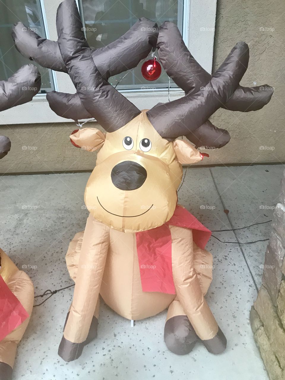 A little Christmas reindeer sitting outside on the front porch with red Christmas bulbs that light up. 
