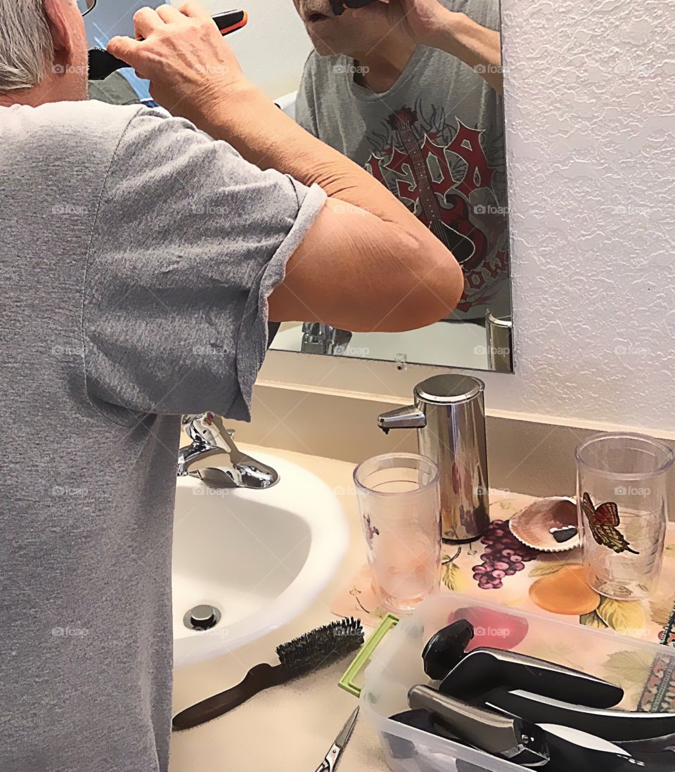 Man shaving and manscaping in the mirror as a ritual every day.