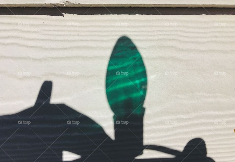 Colorful green shadow from the glass of a Christmas light while putting up the Christmas lights on the house 