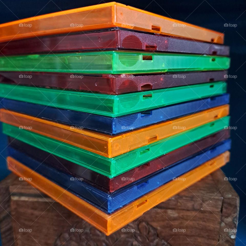 Stack of brightly coloured C.D cases on a wooden box at an angle, close up. Autumnal colours