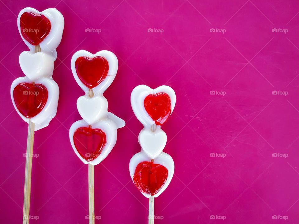 Sweet three Lollipop in the shape of a red and white heart on a pink background with copy space