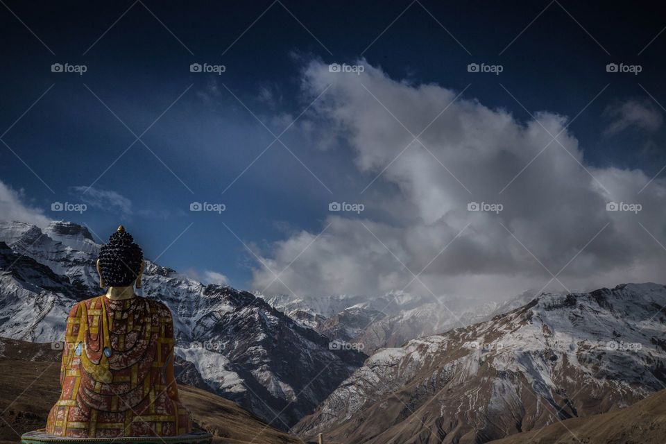 Sitting buddha overlooking open mountains and land with clouds above