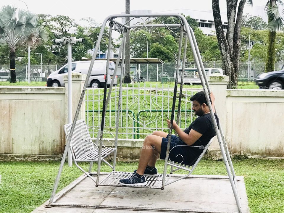 Man swinging on swing outside and watching phone 