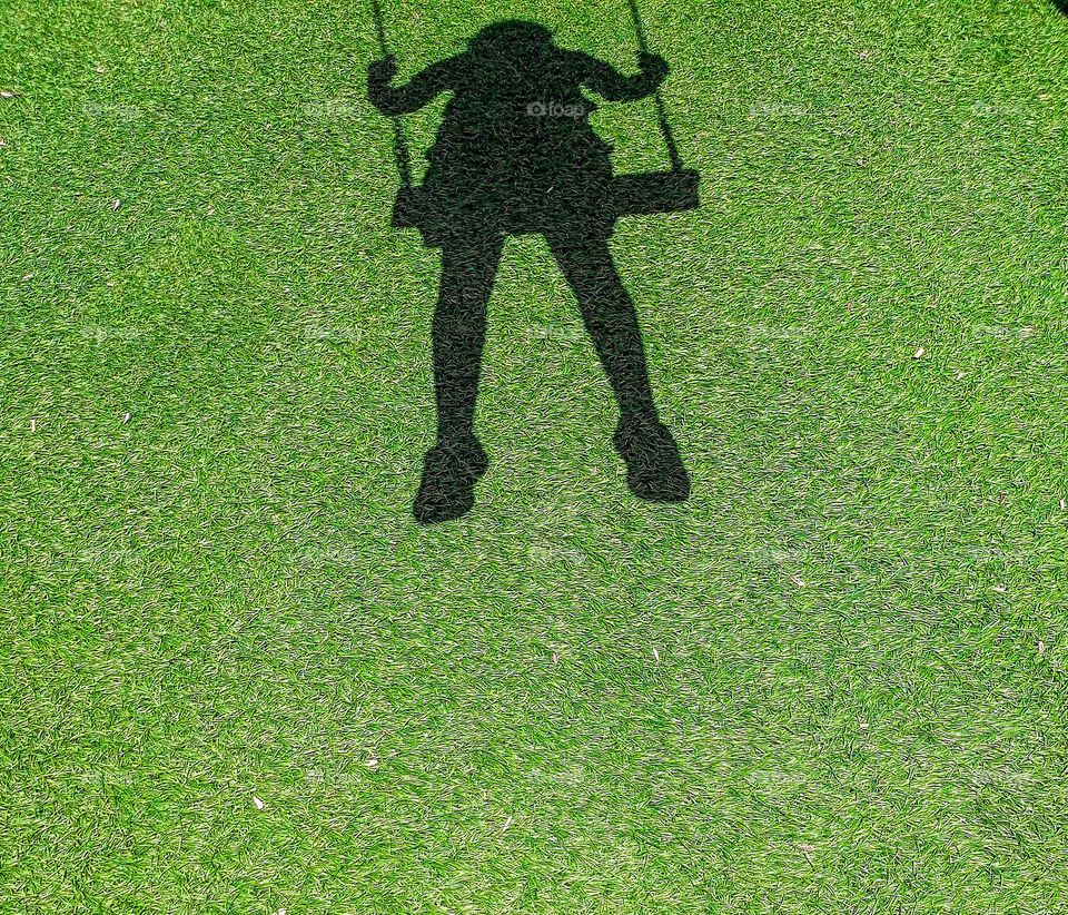 the shadow of a girl swinging at midday