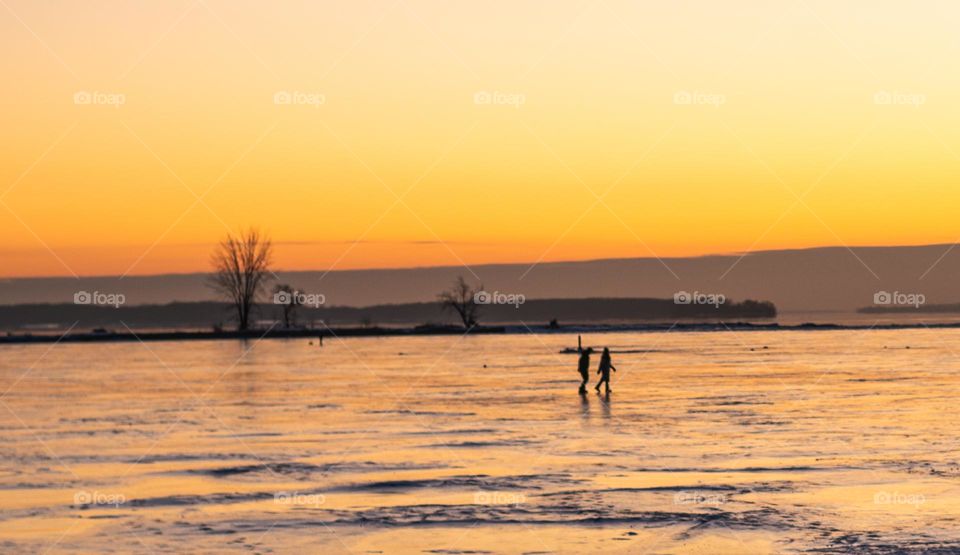 Couple walking on frozen lake at sunset with golden sky 