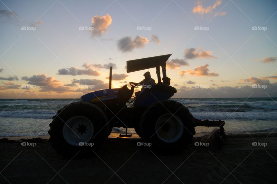 A large tractor is silhouetted against the morning sunrise as it clears seaweed off of the beach in Hollywood, Florida.  