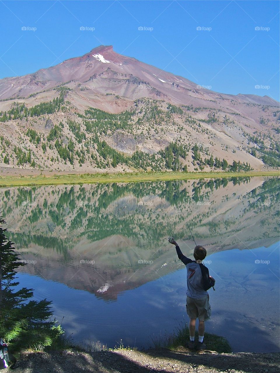 Mountain Reflection. Young man fishing in mountain lake
