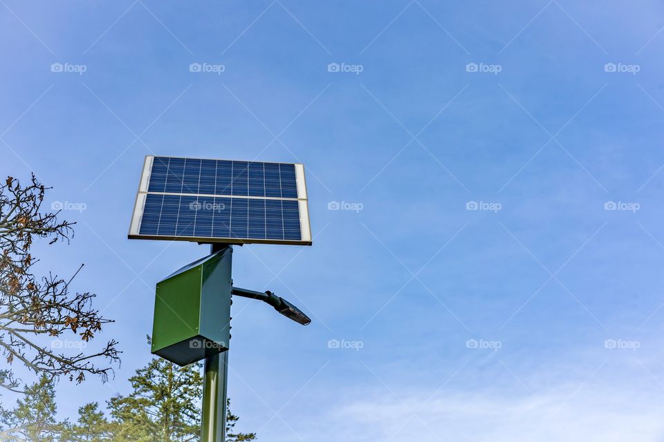 Solar panel, high above a street, takes in the sun’s rays and provides energy for a light