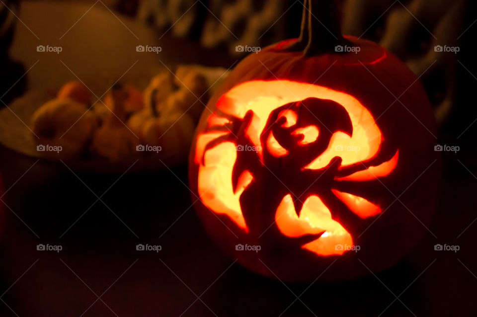 Carved Jack’o lantern pumpkin lit up in home with bowl of little pumpkin decorations on table 