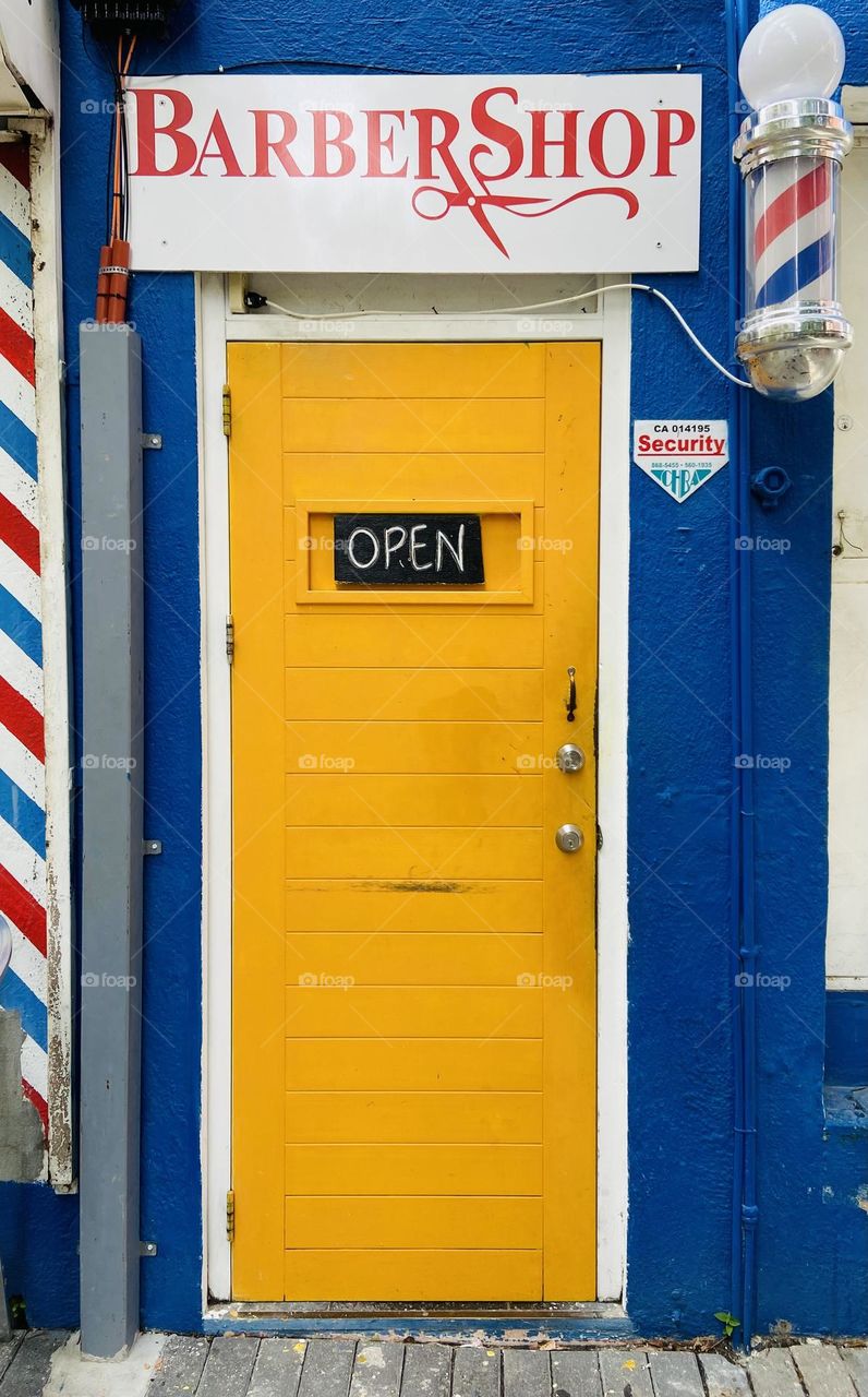 A bright yellow door on a blue building welcoming people in need of a haircut.