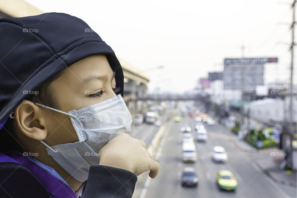 Asean Boys wear a mask to prevent dust Background Blurry car driving on the road and sky train stations.