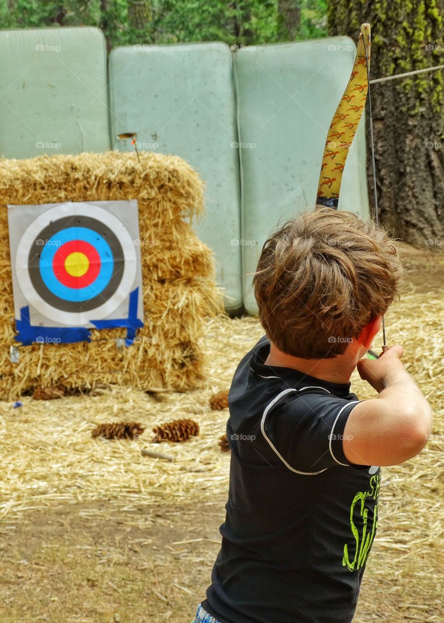 Shooting A Bow And Arrow. Boy Doing Target Practice At The Archery Range