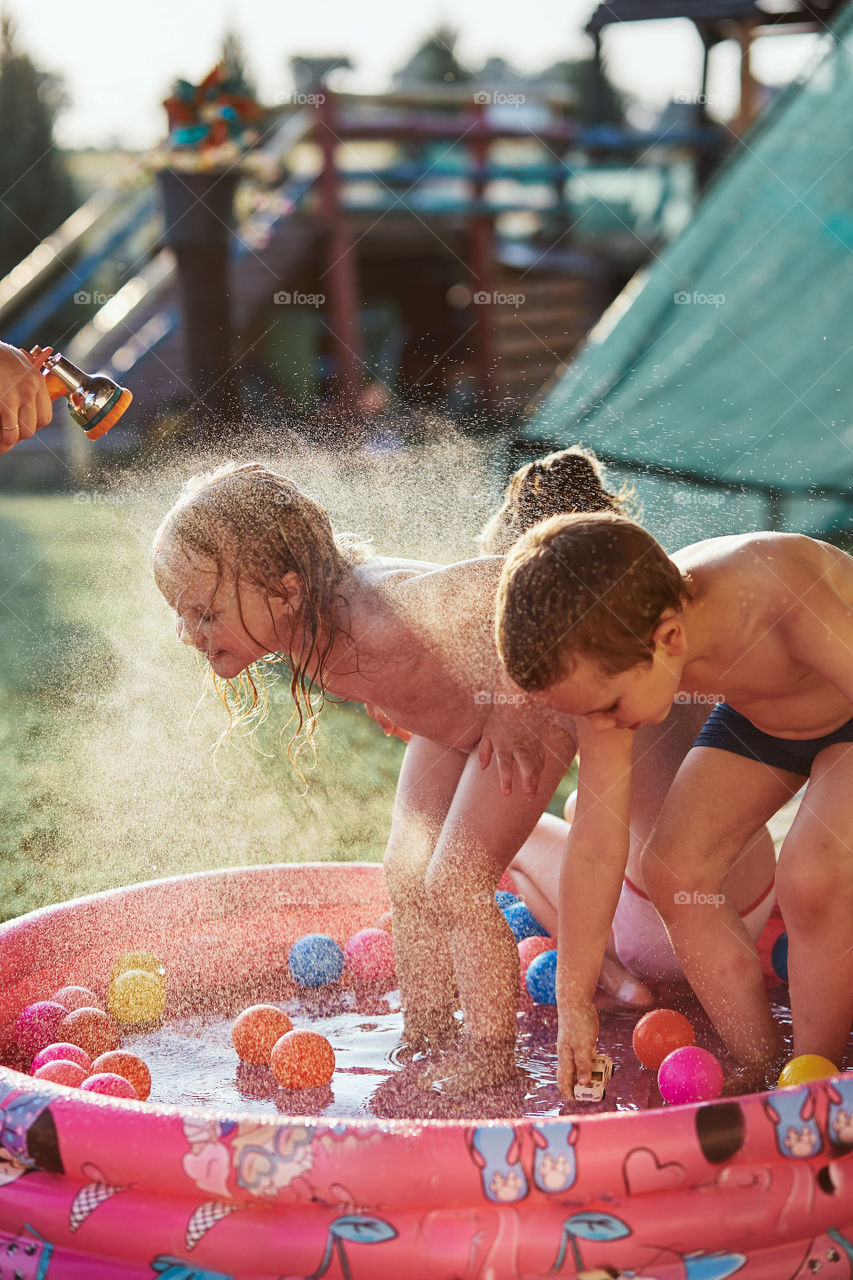 Little cute adorable kids enjoying a cool water sprayed by their father during hot summer day in backyard. Candid people, real moments, authentic situations