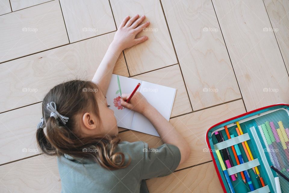 Preschool little girl is sitting on the floor and drawing at bright room at home