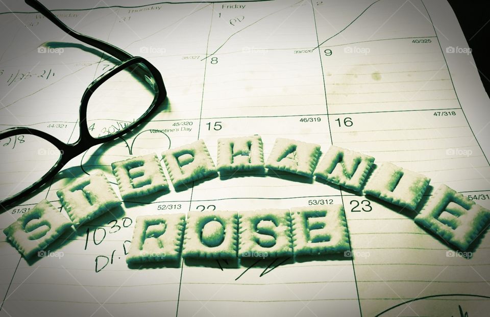 My name spelled out in Scrabble Cheezits next to my glasses on a desk calendar 