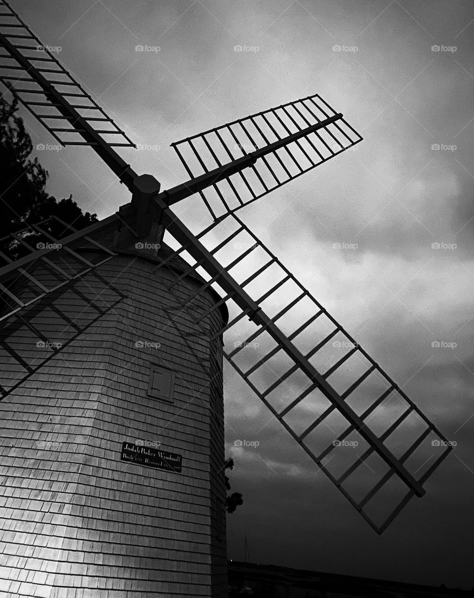 Black and white of a windmill at night, thick clouds in the background. Looking upwards towards her wings. 