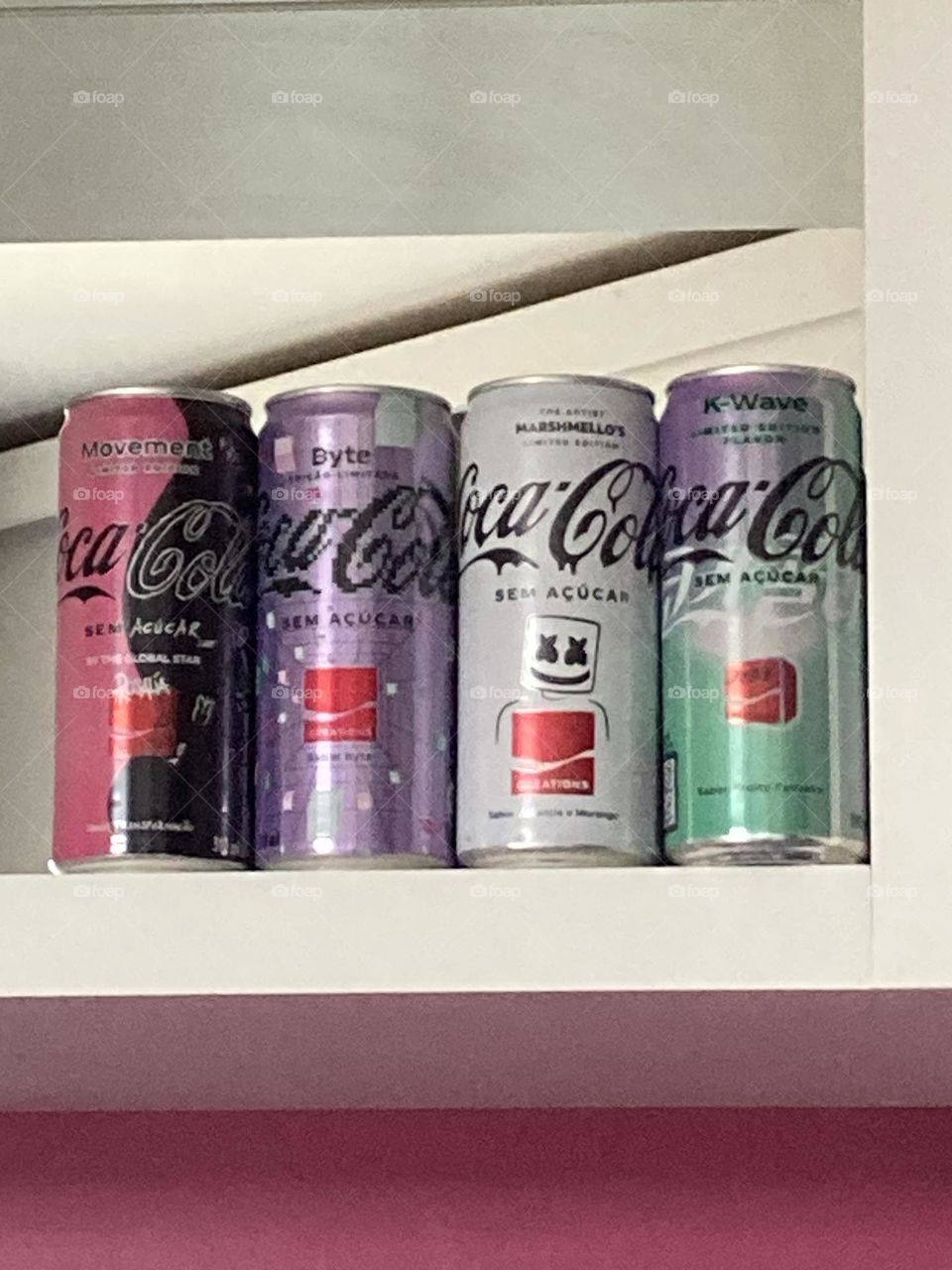 Coleção de latas coloridas com coca cola num nicho branco fixado numa parede cor de beterraba. Amor por latas de coca cola diferentes.