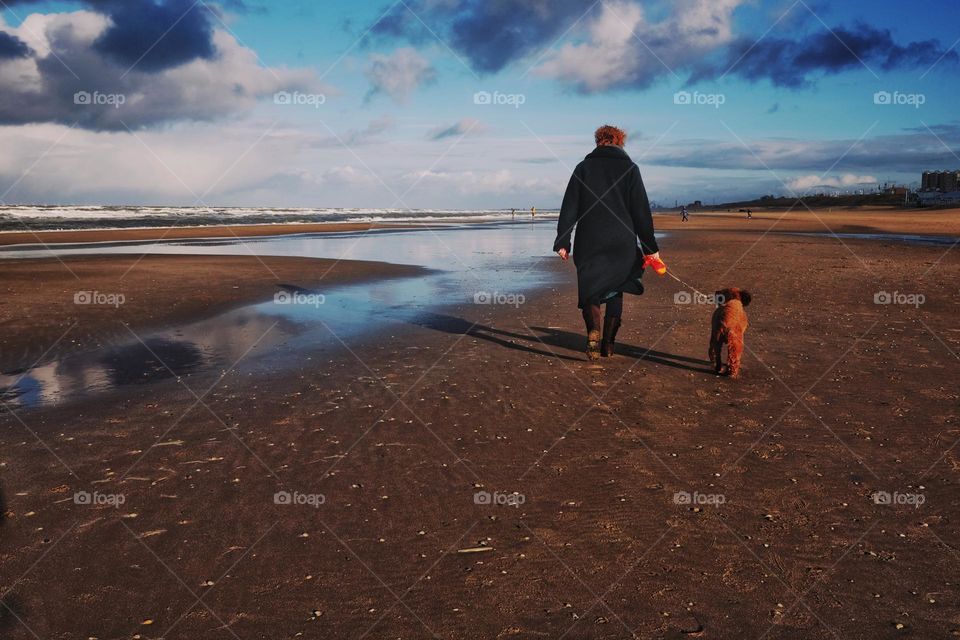 Woman walking with her dog on a sunny day on the beach. Blue skie and clouds