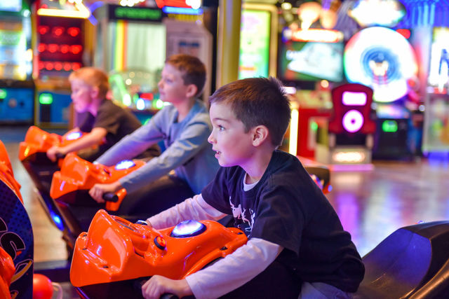 Young boy's face illuminated by the glow of a racing game at an indoor arcade