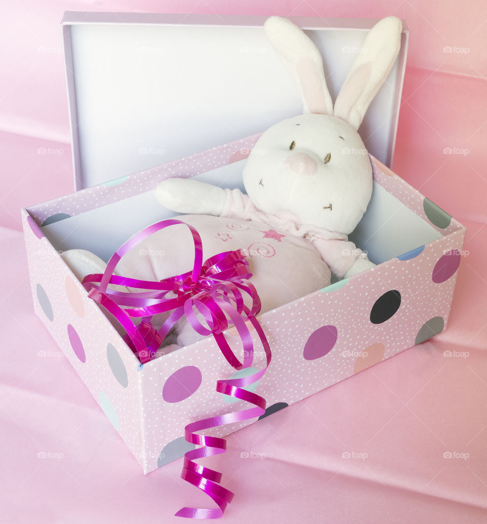 A cute pink soft toy rabbit in a pink spotted gift box with the lid open.