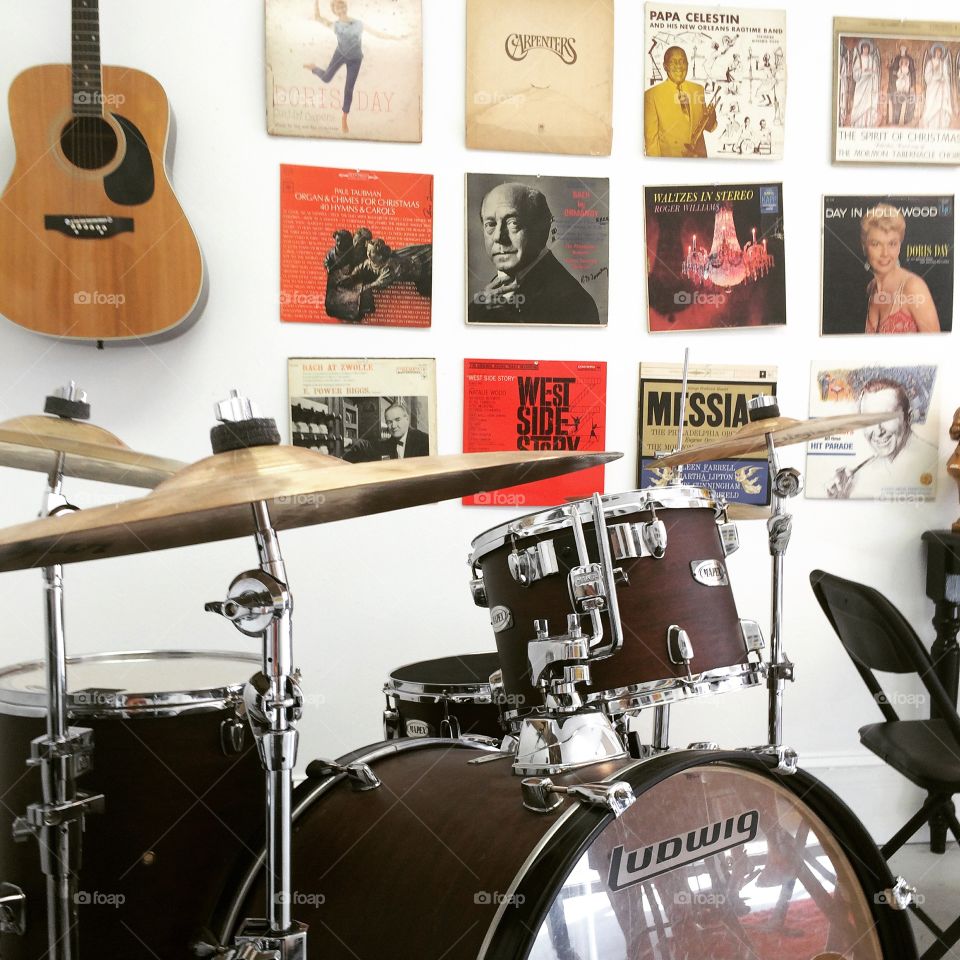 A drum set, antique vinyl records and an acoustic guitar hanging on the wall. Busy music studio.  