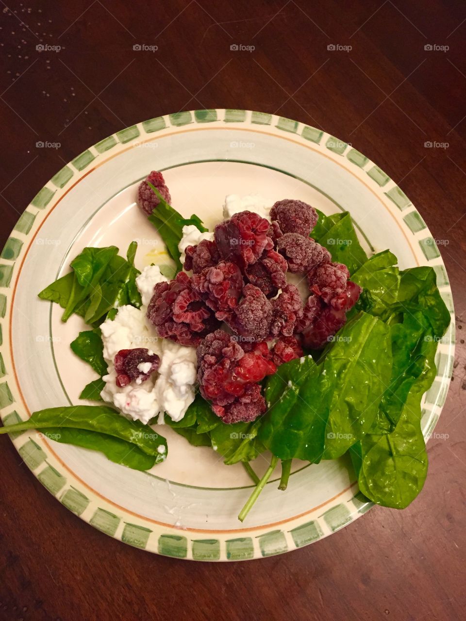 Spinach, raspberries, cottage cheese on a plate poking very colorful  and appetizing.