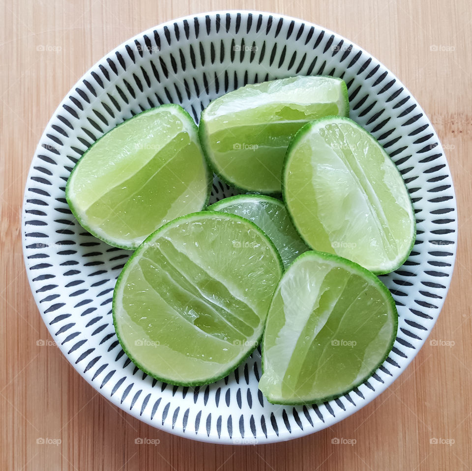 Sliced green limes in a white China porcelain sauce cup, Top view
