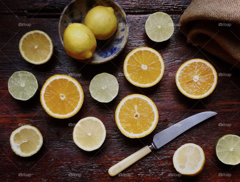 Lemons limes and oranges sliced in half and lying on a rustic wood table with a knife and two whole lemons in a bowl.