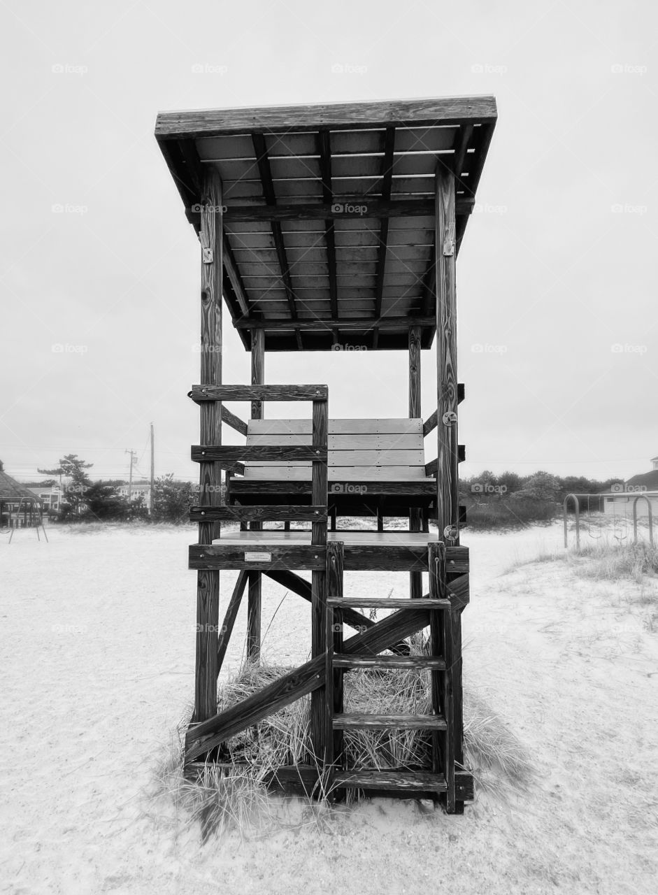 Black and white photo of an empty lifeguard stand on the beach in wintertime.  Stark, focus on foreground, mental health concept 