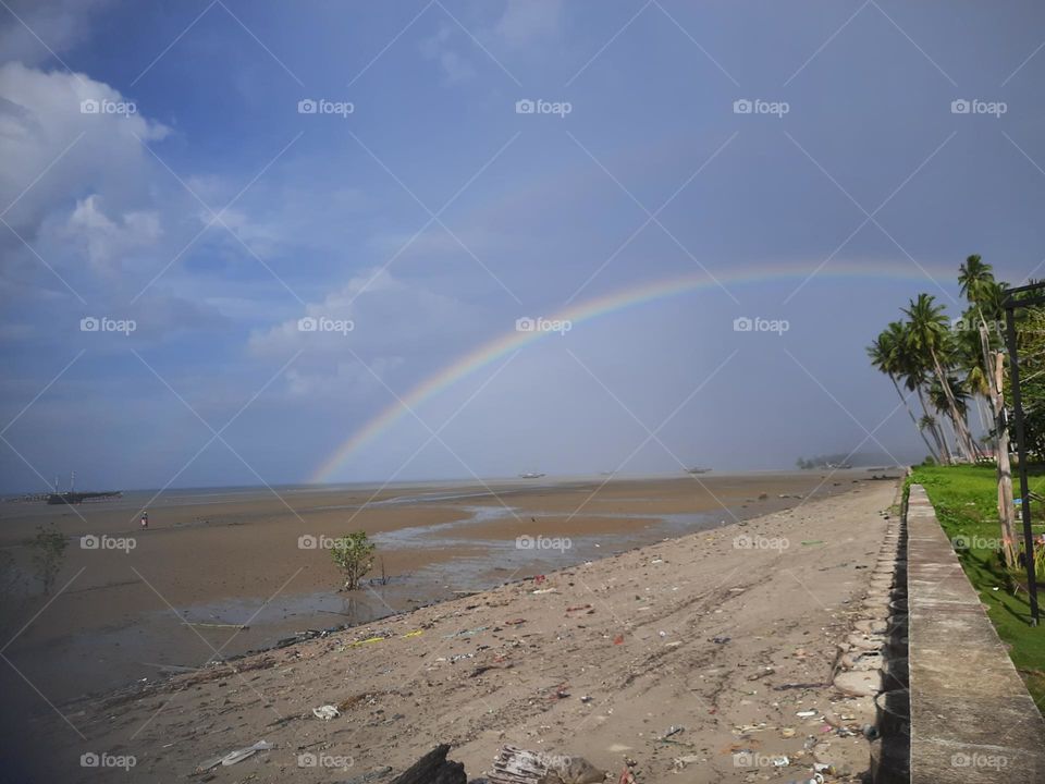 rainbow by the beach on a sunny day and drizzling rain